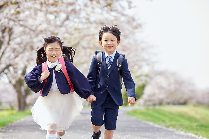 Japanese elementary school students running under cherry blossoms holding hands