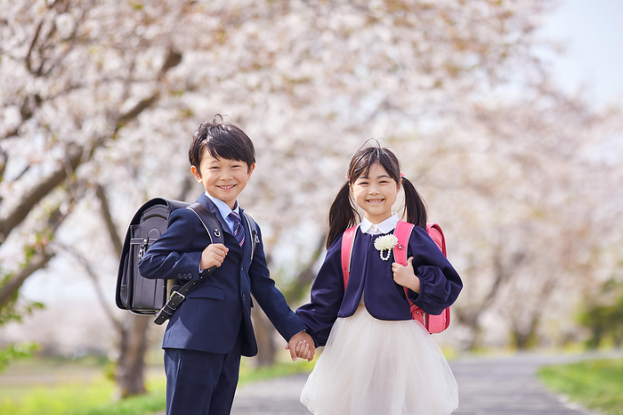 Japanese elementary school students holding hands with under cherry blossoms