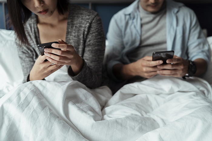 couple Cropped image of two smartphones in couple s hands while they sitting on white bed.