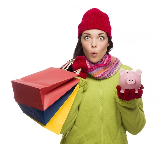 Concerned expressive mixed-race woman wearing winter clothes holding shopping bags and piggybank isolated on white background, Photo by Andy Dean