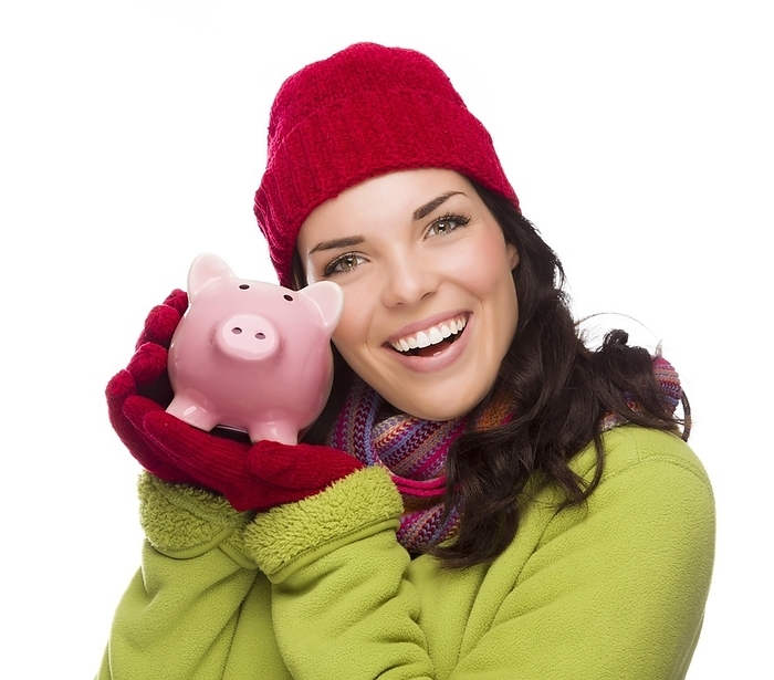 Happy smiling mixed-race woman wearing winter clothing holding piggybank isolated on white background, Photo by Andy Dean