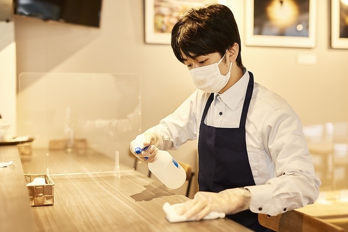 Japanese male waiter sterilizing a table with alcohol