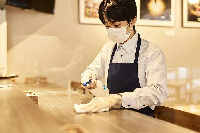 A Japanese male waiter sterilizing a table with alcohol.