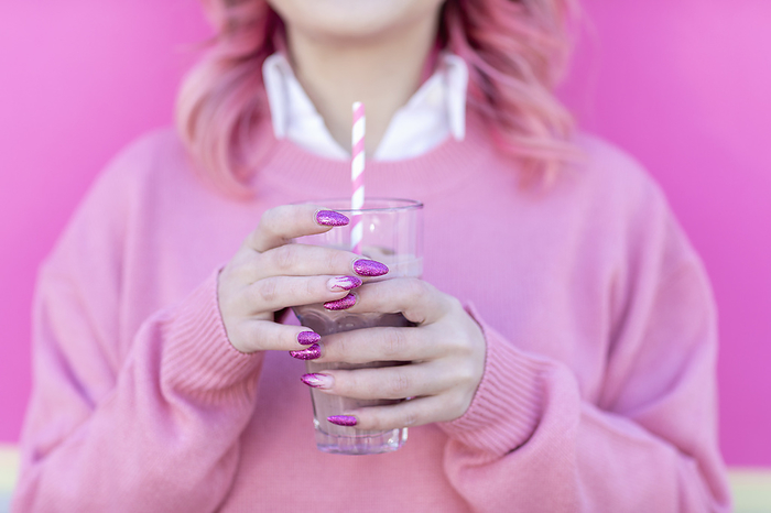 Close up of young woman with pink hair, jumper and glitter nail gel design holding milkshake glass and stripy straw  Florence, Tuscany, Italy Woman with glass of milkshake in front of wall, Photo by Emma Innocenti