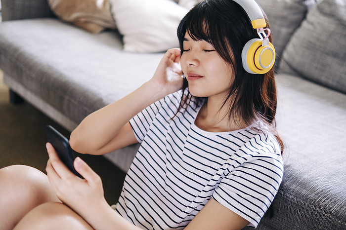 Woman with mobile phone listening music through headphones in living room