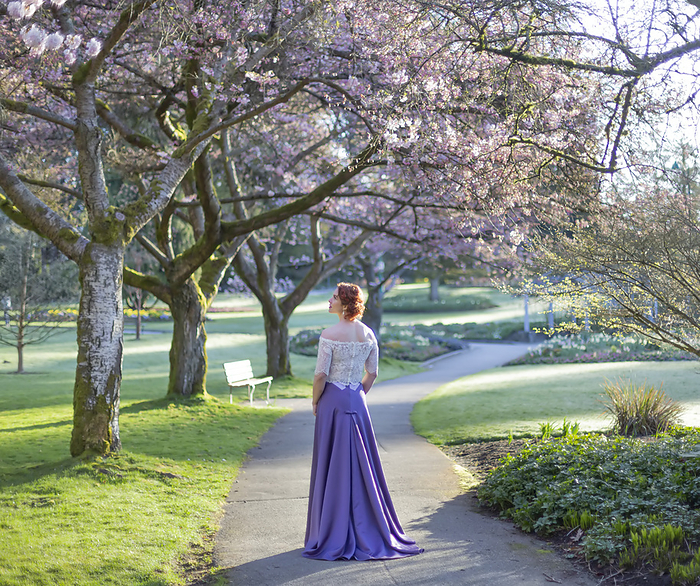 A woman with red curly hair and formal gown standing on a footpath in the gardens of a park; British Columbia, Canada, Photo by Lorna Rande / Design Pics