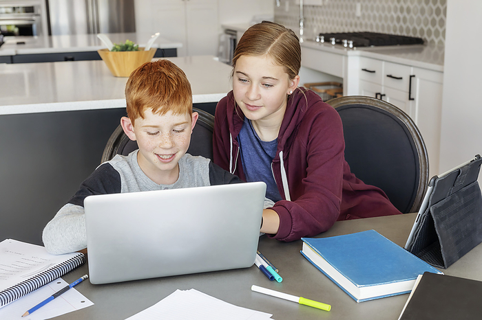 A teenage girl and young boy sit at the kitchen table at home with a laptop and tablet doing school work while being homeschooled; Alberta, Canada, Photo by LJM Photo / Design Pics