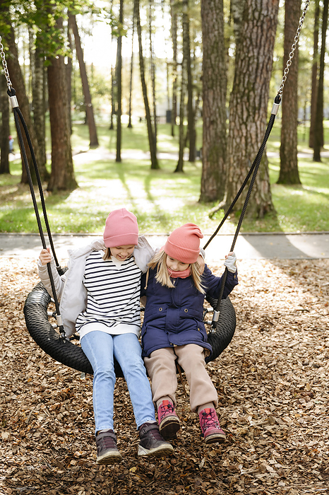 Playful sisters swinging on swing at park