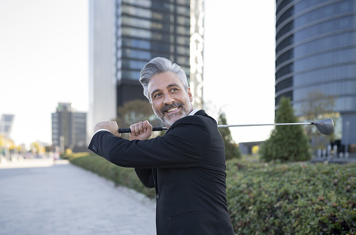 Confident businessman playing golf in city
