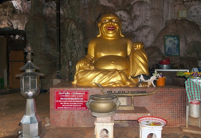 Thailand: Laughing Buddha, Wat Tham Seua, Krabi Town, Krabi Province, Southern Thailand Wat Tham Seua, the  Temple of the Tiger Cave  is built into a cave set in a limestone cliff. br   br    Surrounded by individual monk s residences, this is one of southern Thailand s best known forest temples. br   br    The main viharn or assembly hall extends into a long, shallow limestone cave displaying various grim reminders of mortality as a counterbalance to worldly desires. At the back of the cave a flight of marble stairs lead up to the  tiger cave  itself. Within there is a venerated Buddha footprint on a gilded platform and a life size figure of Ajaan Jamnien, the temple s enigmatic abbot. br   br    The sprawling temple grounds are partly landscaped, and there are two separate stairways leading to a large Guan Yin image  the Mahayana Buddhist version of the Indian sage Avalokitesvara, known generally as  the Chinese Goddess of Mercy  , and to another Buddha footprint.