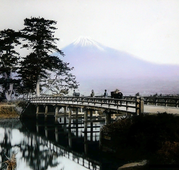 Japan: Crossing a bridge beneath Mount Fuji, T. Enami, c. 1910 T. Enami  Enami Nobukuni, 1859   1929  was the trade name of a celebrated Meiji period photographer. The T. of his trade name is thought to have stood for Toshi, though he never spelled it out on any personal or business document. br   br   br  The T. of his trade name is thought to have  Born in Edo  now Tokyo  during the Bakumatsu era, Enami was first a student of, and then an assistant to the well known photographer and collotypist, Ogawa Kazumasa. Enami relocated to Yokohama, and opened a studio on Benten d ri  Benten Street  in 1892. Just a few doors away from him was the studio of the He and Enami would work together on at least three related projects over the years.  Enami became quietly unique as the only photographer of that period known to work in all popular formats, including the production of large format Enami became quietly unique as the only photographer of that period known to work in all popular formats, including the production of large format photographs compiled into what are commonly called  Yokohama Albums. Enami went on to become Japan s most prolific photographer of small format images such as the stereoview and glass lantern slides. The best of these were delicately hand tinted.