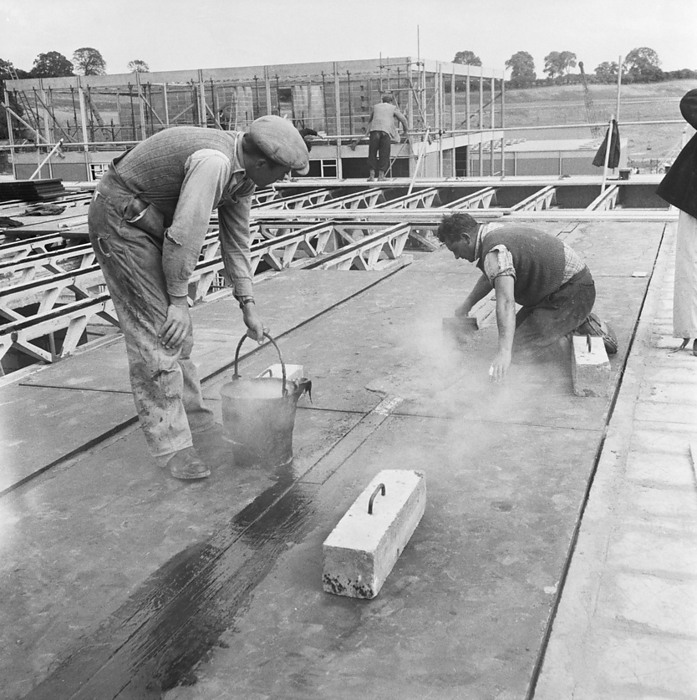County High School, Gedling Road, Arnold, Gedling, Nottinghamshire, 12 09 1958. Creator: John Laing plc. County High School, Gedling Road, Arnold, Gedling, Nottinghamshire, 12 09 1958. Two workers spreading hot tar to seal the joints between roof panels during the construction of Arnold County High School. Work began on the site in March 1958 and construction was completed for the new school term in September 1959.  Laingspan  was a flexible modular system of frame construction using precast pre stressed concrete units. Laing developed the system in conjunction with the Architects and Buildings Branch of the Ministry of Education and consulting engineer AJ Harris. The Arnold school was the first building for which the system was used beyond a prototype extension to Laing s own Research and Development Centre. Designed to economise on steel consumption and minimise on  wet trades  to speed up construction, the system went on to be used for other building types including offices and hospitals.