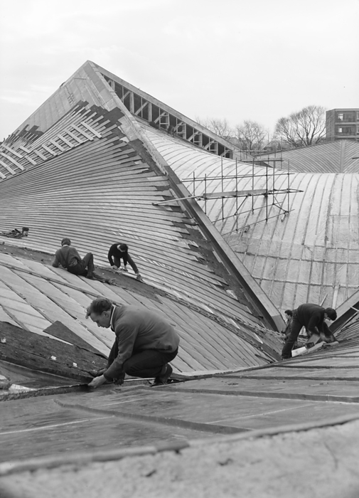 Commonwealth Institute, Kensington High Street, Kensington, London, 06 04 1962. Creator: John Laing plc. Commonwealth Institute, Kensington High Street, Kensington, London, 06 04 1962. Workers laying the outer skin of copper sheeting to weatherproof the exhibition hall roof at the Commonwealth Institute. Laing built the Commonwealth Institute between October 1960 and October 1962 to replace the former Imperial Institute that was to be demolished to make way for new facilities at Imperial College.  The building  consisted of a four storey administrative block housing a library, restaurant, board room and conference hall and a separate two storey block containing a cinema with an art gallery above, but the focus of the project was the exhibition hall with its hyperbolic paraboloid roof, the first of its kind constructed in Great Britain.  The exhibition, designed by James Gardner, provided spaces where each of the Commonwealth nations could showcase their achievements and characteristics, primarily to school children as teaching aids to enliven history and geography lessons. The shell arch of the central roof section was of reinforced concrete, cast in situ using timber formwork with rough sawn boards to provide a textured internal surface whilst the four outer  quot warps quot  were constructed using precast beams and wood wool slabs, blocks of shredded timber bound together in a cement paste and left visible from the interior.  The entire roof was then clad in copper sheeting over a layer of vermiculite.  It covers an area of 33,700sqft, 183 feet square with the central section 93 feet square and ranges between 30ft high at its lowest and 80ft at the peaks.