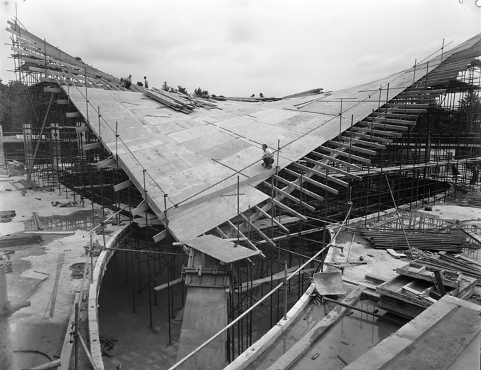 Commonwealth Institute, Kensington High Street, Kensington, London, 27 07 1961. Creator: John Laing plc. Commonwealth Institute, Kensington High Street, Kensington, London, 27 07 1961. Workers constructing the timber formwork for the central hyperbolic paraboloid roof section of the exhibition hall at the Commonwealth Institute. Laing built the Commonwealth Institute between October 1960 and October 1962 to replace the former Imperial Institute that was to be demolished to make way for new facilities at Imperial College.  The building  consisted of a four storey administrative block housing a library, restaurant, board room and conference hall and a separate two storey block containing a cinema with an art gallery above, but the focus of the project was the exhibition hall with its hyperbolic paraboloid roof, the first of its kind constructed in Great Britain.  The exhibition, designed by James Gardner, provided spaces where each of the Commonwealth nations could showcase their achievements and characteristics, primarily to school children as teaching aids to enliven history and geography lessons. The shell arch of the central roof section was of reinforced concrete, cast in situ using timber formwork with rough sawn boards to provide a textured internal surface whilst the four outer warps were constructed using precast beams and wood wool slabs, blocks of shredded timber bound together in a cement paste and left visible from the interior.  The entire roof was then clad in copper sheeting over a layer of vermiculite.  It covers an area of 33,700sqft, 183 feet square with the central section 93 feet square and ranges between 30ft high at its lowest and 80ft at the peaks.