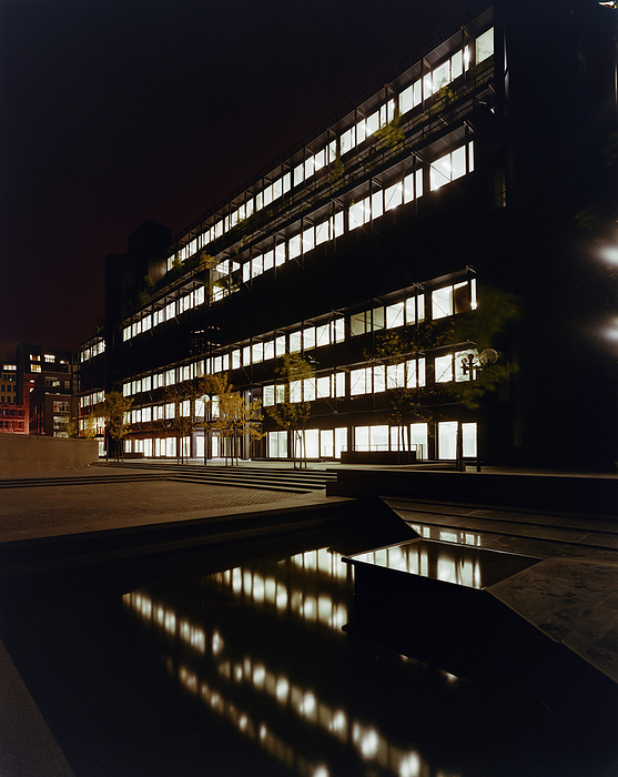 1 Finsbury Avenue, Broadgate, City of London, 03 09 1984. Creator: John Laing plc. 1 Finsbury Avenue, Broadgate, City of London, 03 09 1984. A night scene with the lights from the office block at 1 Finsbury Avenue reflected by the pool in front. The Finsbury Avenue complex was a three phase speculative office development by Rosehaugh Greycoat Estates in anticipation of the deregulation of the financial markets in 1986.  It aimed to entice potential tenants in the financial services industry to a fringe area on the edge of the City through high quality design and construction.  Designed by Peter Foggo of Arup Associates, Laing secured the management contract for the construction of each phase in turn.  Work on phase one, 1 Finsbury Avenue began in December 1982 and was completed by September 1984 followed by phase two, 3 Finsbury Avenue, from October 1985 to December 1986 with work beginning on phase three, 2 Finsbury Avenue in January 1987 and complete by April 1988.  The design for each of the three buildings followed a  quot shell and core quot  approach incorporating flexibility in the internal construction and allowing simple reconfiguration of space according to tenants needs.  Laing undertook several contracts to refit office space in each of the buildings in subsequent years. 1 Finsbury Avenue is constructed around a central atrium with an octagonal glazed lantern roof providing daylight to the office space on all floors and in contrast to expectations from the dark bronze anodised aluminium and tinted windows of the exterior.  The roof terraces  x2019  stepped design and the brises soleil with diagonal bracing breaks up the silhouette and fa  xe7 ade of the building and mitigate the impact of its size.  The building became almost a blueprint for future developments of this kind.  It won a RIBA design award in 1987 and was listed grade II in 2015.