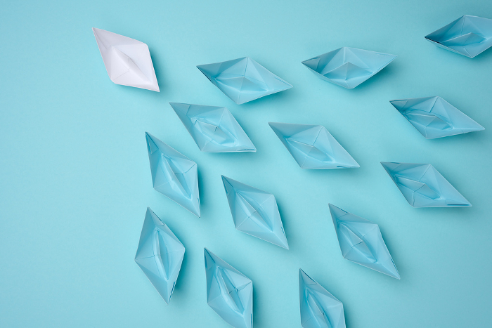 a group of blue paper boats follow white against a light blue ba a group of blue paper boats follow white against a light blue background. Strong leader concept, mass manipulation. Starting a business with a well coordinated team, start up