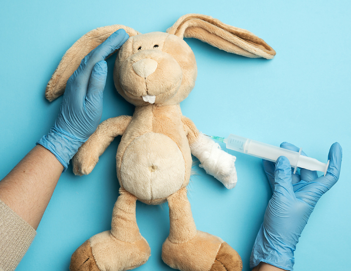 plush rabbit with a bandaged paw and two female hands of a doctor injecting an injection on a blue background, the concept of vaccination and treatment plush rabbit with a bandaged paw and two female hands of a doctor injecting an injection on a blue background, the concept of vaccination and treatment
