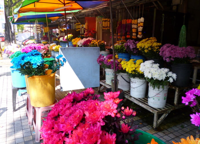 A florist in front of a temple with chemically dyed flower offerings, George Town, Penang Island.