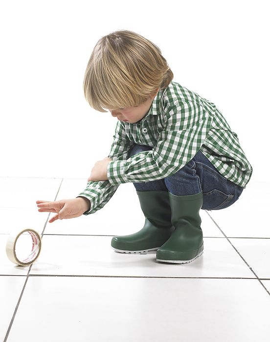 Boy crouching next to roll of tape Boy crouching next to roll of tape, 2 years., Photo by DK IMAGES SCIENCE PHOTO LIBRARY