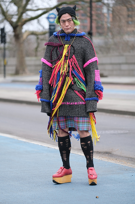 Fall Winter 2022 23 London Street Snapshot Street style on day 4 of London Fashion Week on Monday 21st February 2022. Stylish individuals are seen arriving to their shows or presentations. Image shows flamboyant Japanese Journalist Yu Masui. He wears a long knitwear sweater by Roksanda ilincic, with a tartan skirt or kilt and shoes both by Vivienned Westwood. 