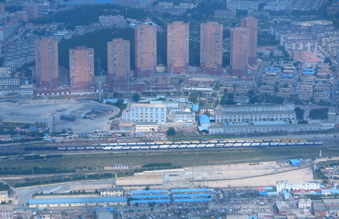 Aerial view of Dalian's railroad tracks lined with freight trains and the city center from above (aerial view through the window of a passenger plane).