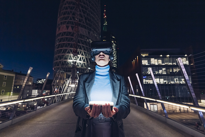 Businesswoman with virtual reality headset holding LED light on bridge in city, Photo by Eugenio Marongiu