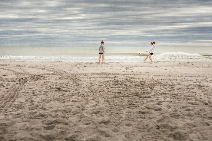 Two girls in hoodies play soccer on a deserted Florida beach in winter, Cocoa Beach, Florida, United States
