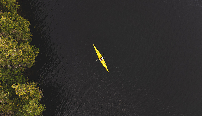 Aerial view of woman paddling yellow kayak on dark lake water., Buck Lake, Ontario, Canada