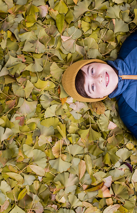 Overhead of happy boy laying on a pile of yellow leaves on fall day., Kingston, Ontario, Canada