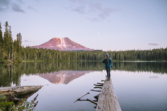 Female standing on a log with Mount Adams reflecting in the lake, Randle, Washington, United States