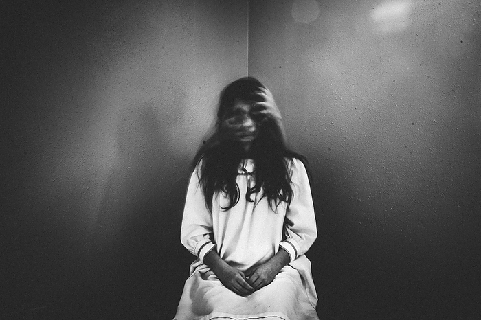 Creepy girl sits in chair with ghostly hands covering her face, Grimes, Iowa, United States