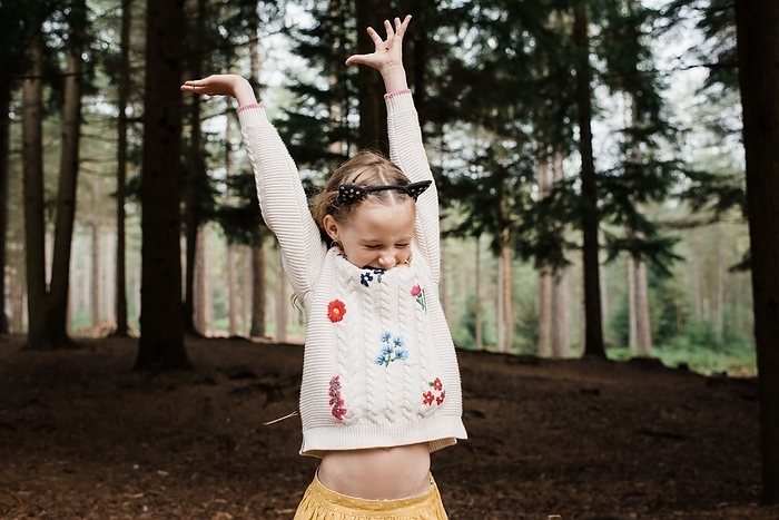 girl throwing twigs up in the air in a forest in autumn, New Forest District, England, United Kingdom
