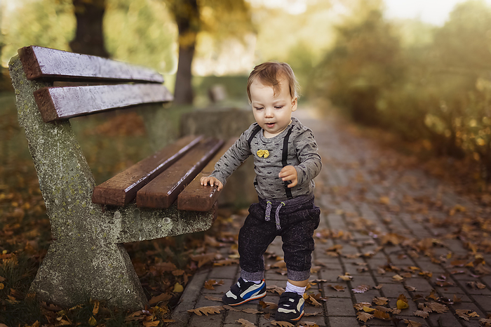 Small baby boy doing his first steps in park while holding bench, Gryfino, West Pomeranian Voivodeship, Poland