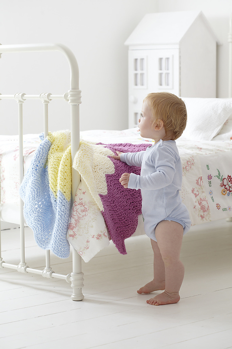 Baby boy standing next to bed Baby boy standing next to bed with knitted blanket draped over the edge, 12 months., Photo by DK IMAGES SCIENCE PHOTO LIBRARY