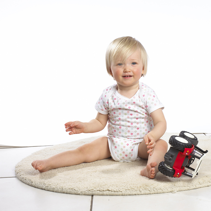 Baby girl Baby girl sitting on rug, toy tractor by her feet., Photo by DK IMAGES SCIENCE PHOTO LIBRARY