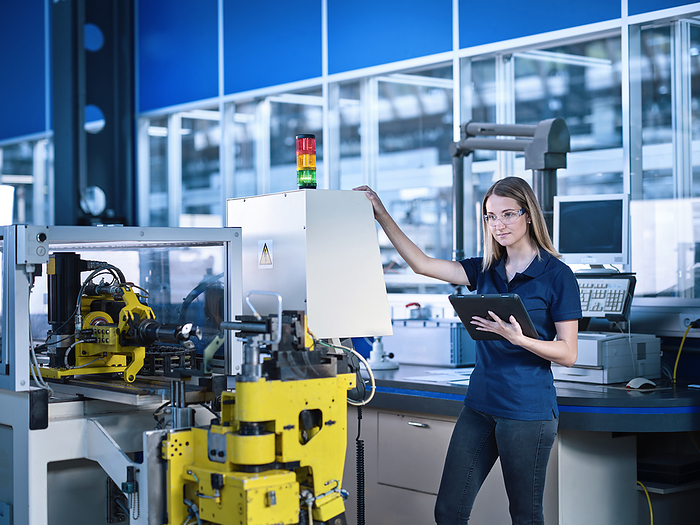 Engineer with tablet PC standing near machine in industry
