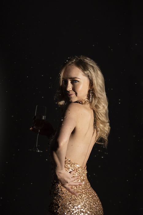 Kaliningrad, Russia. New year party. Young woman in golden sequin cocktail dress with hand on hip against black background