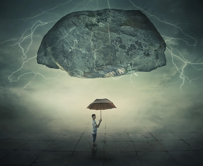 Surrealistic image as a man stand in a foggy street under a huge levitating rock, holding an umbrella in hand as a protection from danger. Life pressure and stress concept, Photo by PsychoShadow