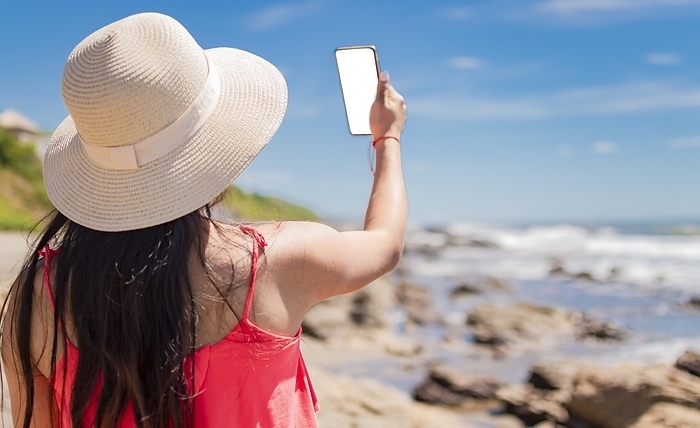 Hat woman taking photos at sea, latin girl taking vacation photos, rear view of girl taking selfie on the beach, Photo by Isai Hernandez