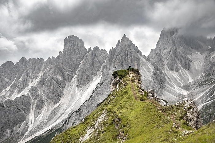 Italy Hiker standing on a ridge, mountain peaks and pointed rocks behind, dramatic cloudy sky, Cimon di Croda Liscia and Cadini group, Auronzo di Cadore, Belluno, Italy, Europe, Photo by Mara Brandl