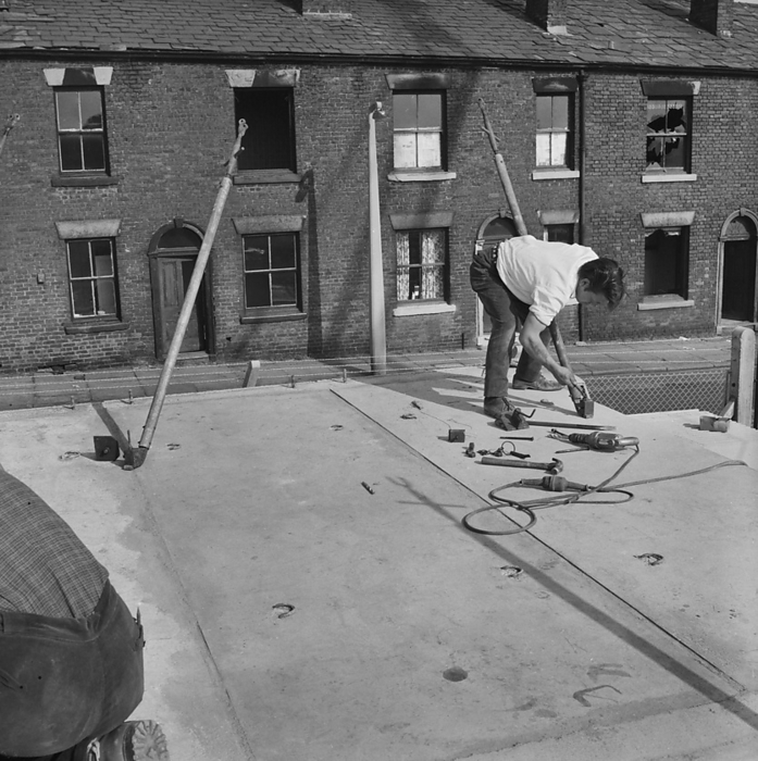 St Mary s Estate, Oldham, 01 09 1964. Creator: John Laing plc. St Mary s Estate, Oldham, 01 09 1964. A worker securing a concrete slab during the construction of 12M Jespersen prototype flats in Oldham, with derelict terraced houses in the background. In 1963, John Laing and Son Ltd bought the rights to the Danish industrialised building system known as Jespersen  sometimes referred to as Jesperson . The company built factories in Scotland, Hampshire and Lancashire producing Jespersen prefabricated parts and precast concrete panels, allowing the building of housing to be rationalised, saving time and money. The prototype flats shown in the photograph were built using the 12M Jespersen building system and were the first to be erected in Britain by Laing for the County Borough of Oldham. They were a short distance from the future St Mary s Estate on which 500 dwellings were due to be built comprising of low rise flats and modern terraced houses, replacing the earlier slums which had occupied the area. The 12M Jespersen flats on the housing estate were later demolished in 2007 with only the houses left standing.