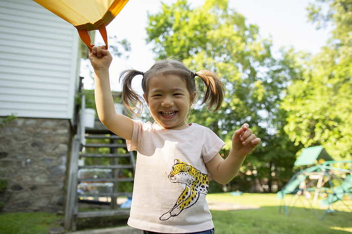 Happy Young Child Smiles While Holding Parachute in Backyard