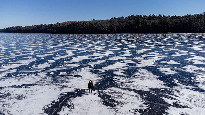 Aerial view of a person walking on a frozen snow covered lake.