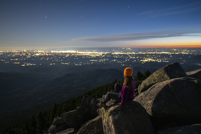 Female sitting on boulders at night above the city lights below