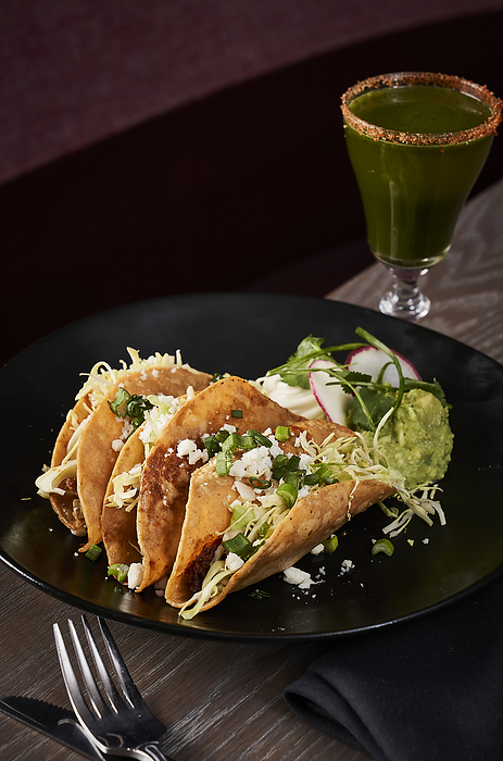 Hard shelled tacos with guacamole and a craft cocktail .