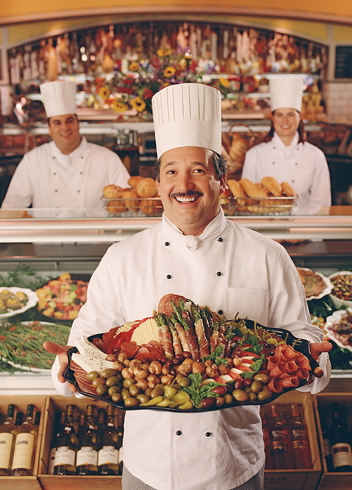 Associate in Chefs hat at deli counter with large selection of imported meats and cheeses  Associate in Chefs hat at deli counter with large selection of imported meats and cheeses