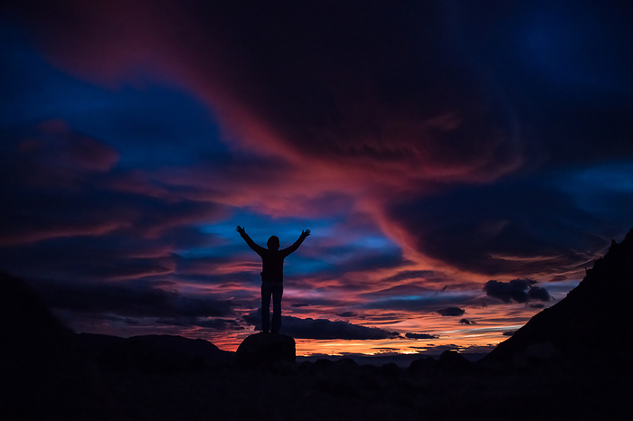 Argentina Hiker with arms raised in air looking out at sunset in Patagonia, Chile.