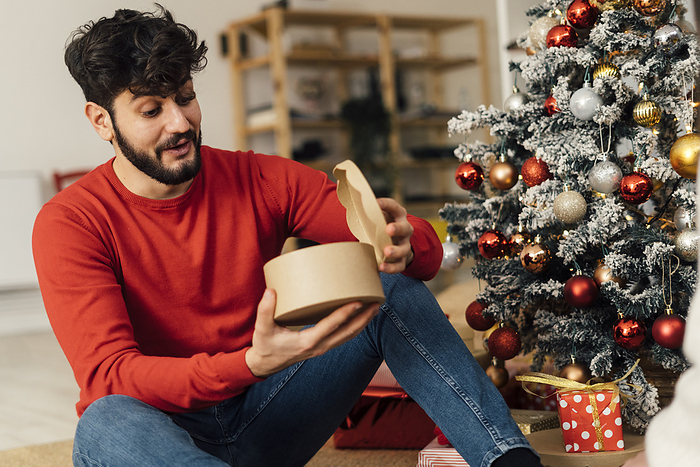 Surprised young man opening Christmas present at home