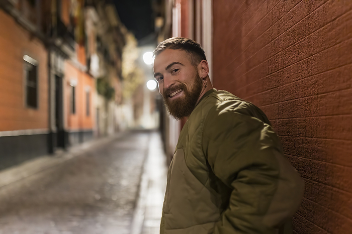 Smiling young man with beard standing in front of wall