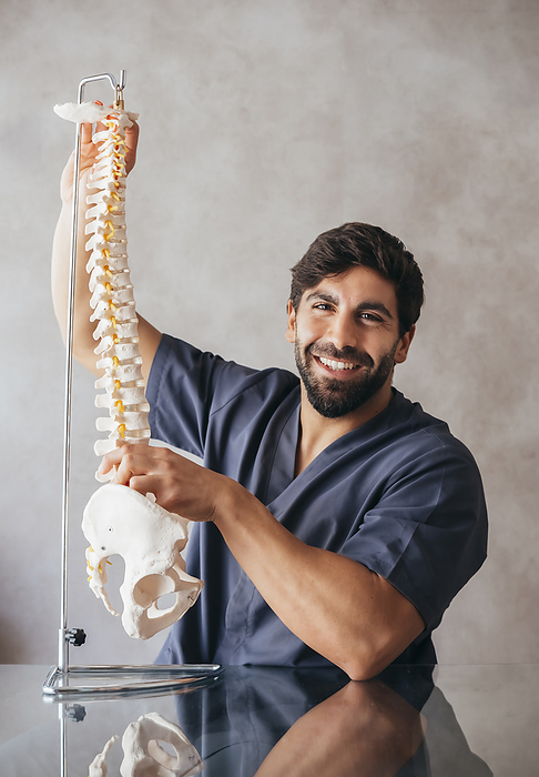 Smiling physiotherapist holding human spine model